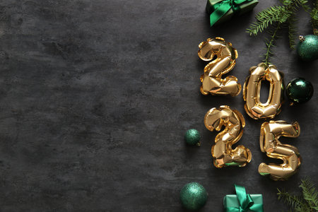 Figure 2025 made of foil balloons with Christmas balls, gift boxes and fir branches on black...