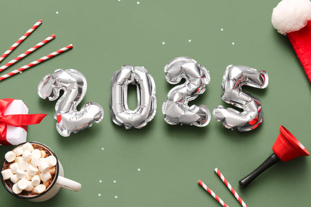 Figure 2025 made of foil balloons with Christmas bell, gift box and cup of cocoa on green backgroundの写真素材