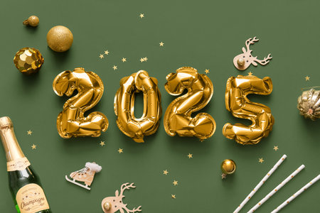 Figure 2025 made of foil balloons with Christmas decorations and bottle of champagne on green backgroundの写真素材