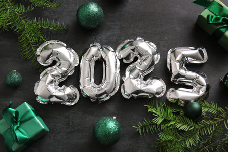 Figure 2025 made of foil balloons with Christmas balls, gift boxes and fir branches on black...
