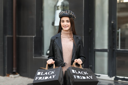 Beautiful young happy woman with shopping bags near clothing store on city street. Black Friday saleの写真素材