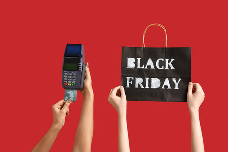Hands with payment terminal and shopping bag on red background. Black Friday sale