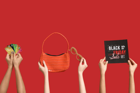 Hands holding bag, sunglasses, credit cards and paper with text BLACK FRIDAY SALE on red backgroundの写真素材