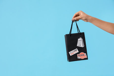 Female hand with shopping bag on blue background. Black Friday saleの写真素材