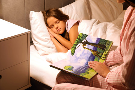 Mother reading fairy-tale for her sleeping little daughter in bed at night