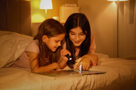 Happy mother and her little daughter with flashlight reading fairy-tale in bed at night