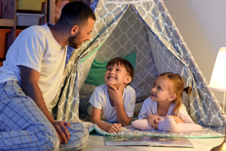 Father and his cute little children in play tent reading book before going to sleepの写真素材