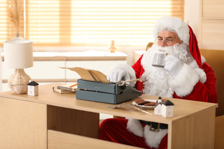 Santa Claus with typewriter and cup of hot cacao writing Christmas story at homeの写真素材