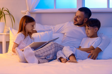 Young man reading bedtime story to his children in bedの写真素材