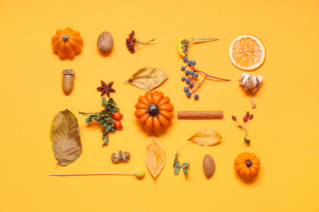 Candles in shape of pumpkin, autumn leaves and berries on yellow background