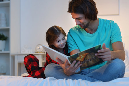 Father reading book for his little daughter in bedの写真素材