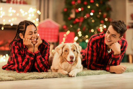Happy young couple in pajamas with dog lying at home on Christmas Eveの写真素材
