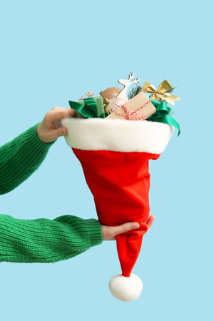 Woman holding Santa hat with Christmas gifts and decorations on color background, closeupの写真素材