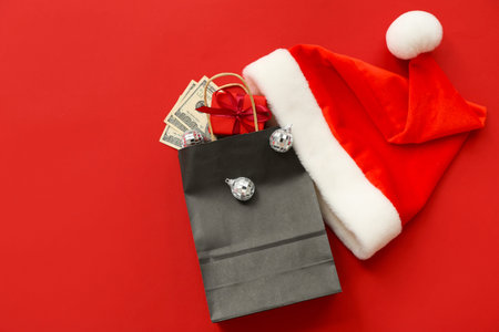Composition with Santa hat, paper shopping bag, Christmas decorations and money on red backgroundの写真素材
