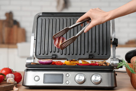 Woman cooking vegetables on modern electric grill in kitchenの写真素材
