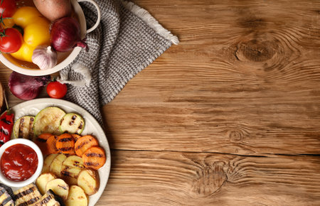 Plate with grilled vegetables and bowl with sauce on wooden backgroundの写真素材