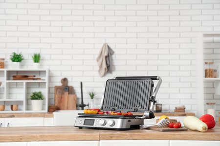 Modern electric grill with vegetables on wooden table in kitchenの写真素材