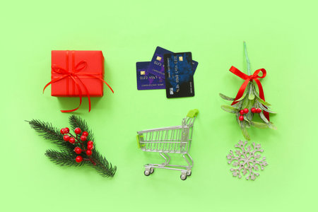 Composition with mini shopping cart, Christmas gift, decorations and credit cards on green...