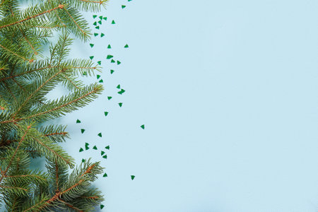Christmas tree branches and confetti on blue background
