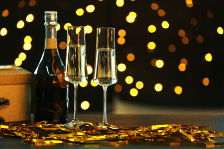 Bottle of champagne with glasses, Christmas gift box and serpentine on table against blurred lightsの写真素材