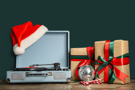 Vinyl record player with disc, Santa hat, disco ball, candy canes and Christmas gift boxes on wooden tableの写真素材