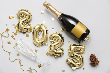 Figure 2025 made of balloons with bottle of champagne, glass and Christmas decor on white background