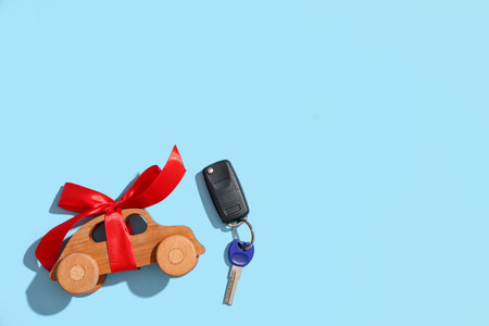 Keys of new car and wooden toy tied with red ribbon on color backgroundの写真素材