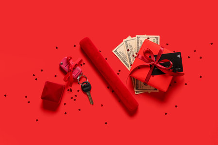 Composition with gift box, money, keys of new car and jewelry boxes on red backgroundの写真素材