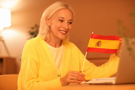 Mature woman with flag of Spain learning language online at home in eveningの写真素材