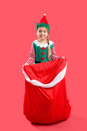 Cute little girl in elf costume with Santa bag on red background