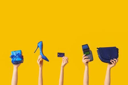 Many female hands with accessories, payment terminal and Christmas gift box on yellow backgroundの写真素材