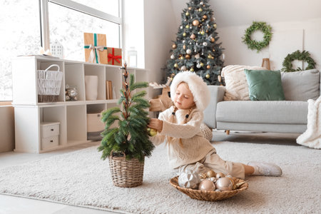 Cute little girl in Santa hat decorating Christmas tree at homeの写真素材