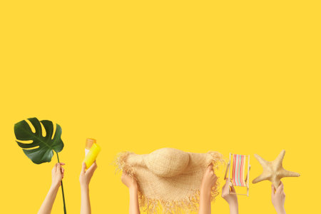 Female hands with straw hat, mini deck chair, starfish, sunscreen cream and monstera leaf on yellow background. Travel conceptの写真素材