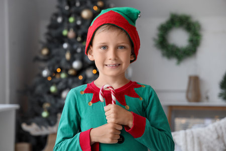 Cute happy little boy dressed as Christmas elf with candy cane at homeの写真素材