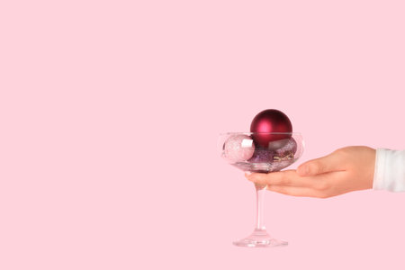 Female hand with glass of beautiful Christmas balls on pink background, closeupの写真素材