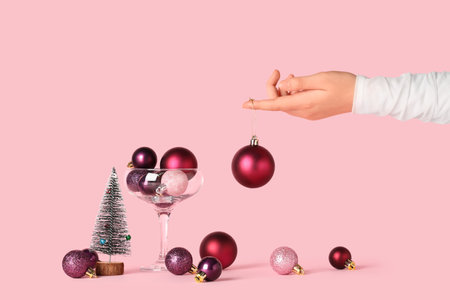 Female hand with beautiful Christmas balls on pink backgroundの写真素材