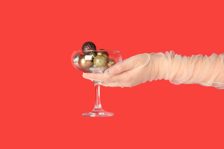 Female hand in laced glove with glass of Christmas balls on red background, closeupの写真素材