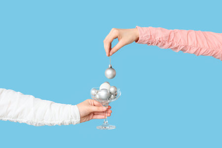 Female hands with glass of Christmas balls on color backgroundの写真素材