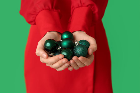 Woman in stylish red dress holding beautiful Christmas balls on green background, closeupの写真素材