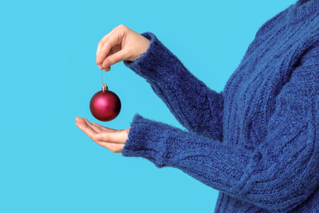 Woman in warm knitted sweater holding beautiful Christmas ball on color background, closeupの写真素材