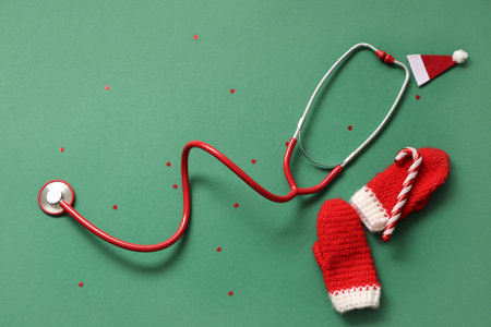 Stethoscope with decorative Christmas hat and knitted mittens on green backgroundの写真素材