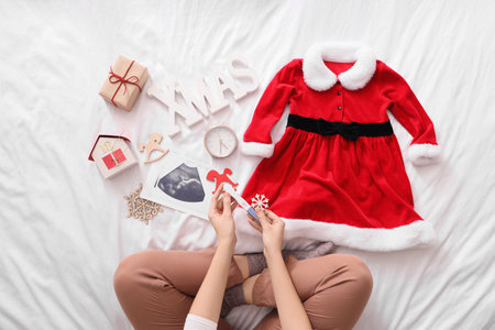Young pregnant woman with pregnancy test, sonogram image and Christmas decorations sitting on bed, top viewの写真素材
