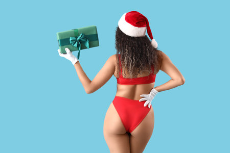 Sexy young African-American woman in swimsuit with Christmas gift box on blue background, back viewの写真素材
