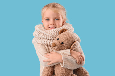 Cute little girl in winter clothes with toy bear on blue backgroundの写真素材