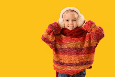 Cute little girl in winter clothes on yellow backgroundの写真素材