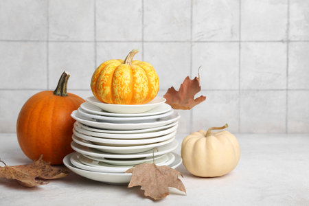 Stack of dishes with autumn decor and pumpkins on table against white tile backgroundの写真素材