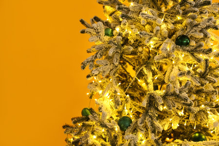 Decorated Christmas tree with glowing lights and baubles near yellow wall, closeupの写真素材