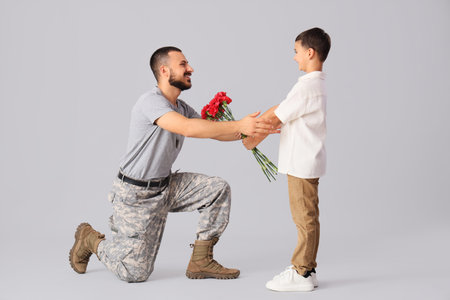 Male soldier receiving flowers from his little son on light background. Veterans Day celebrationの写真素材