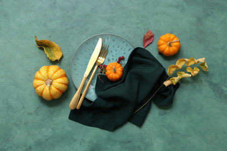Beautiful table setting with fresh pumpkins, rose hip berries and autumn leaves on green backgroundの写真素材