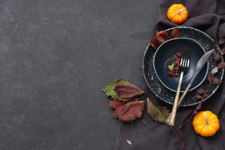 Beautiful table setting with fresh pumpkins, rose hip berries and autumn leaves on black backgroundの写真素材